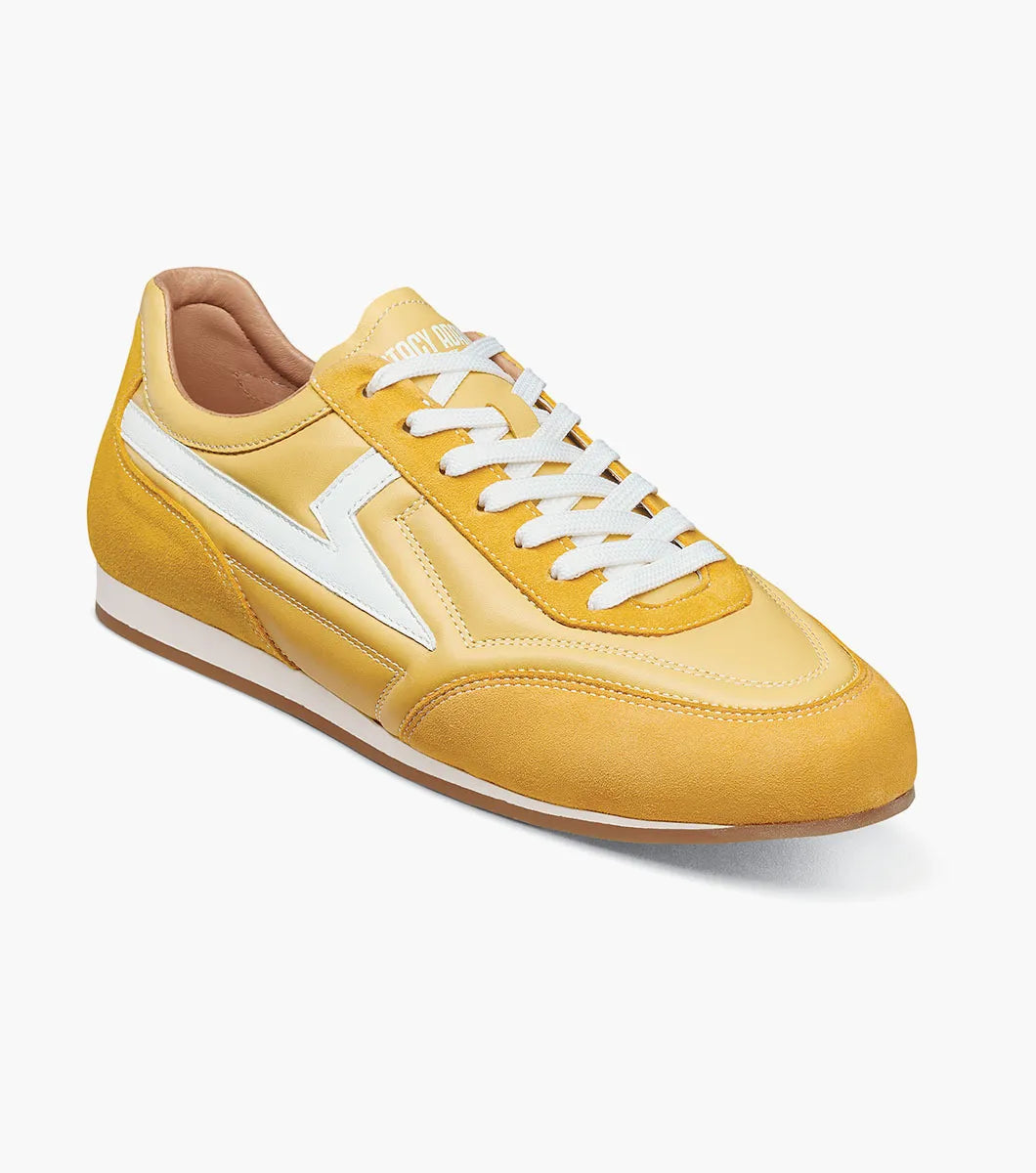 Introducing the Stacy Adams Action 150 Sporty Lace Up sneaker in yellow (Style 25797-700) by STACY ADAMS. This modern shoe features white laces, a white zigzag stripe on the side, tan lining, and a flat white sole. Angled to display both the side and front, it showcases its contemporary design and cushioned footbed for all-day comfort.
