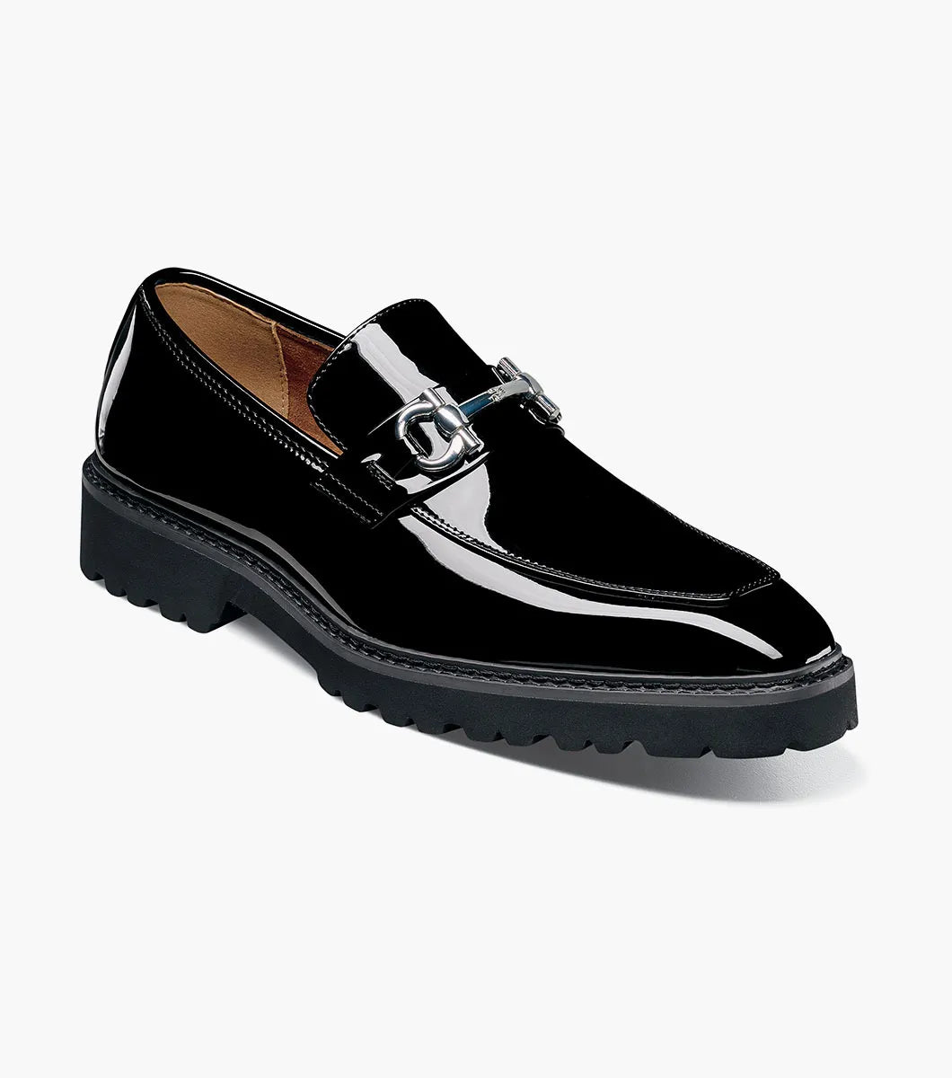 The STACY ADAMS Carabello Moc Toe Bit Slip On (Black Patent, style 25804-004) features a glossy black patent leather upper, a chunky rubber sole, and a sleek metallic bit detail across the front. Designed with a cushioned insole for added comfort, this effortlessly stylish dress shoe is displayed against a white background.