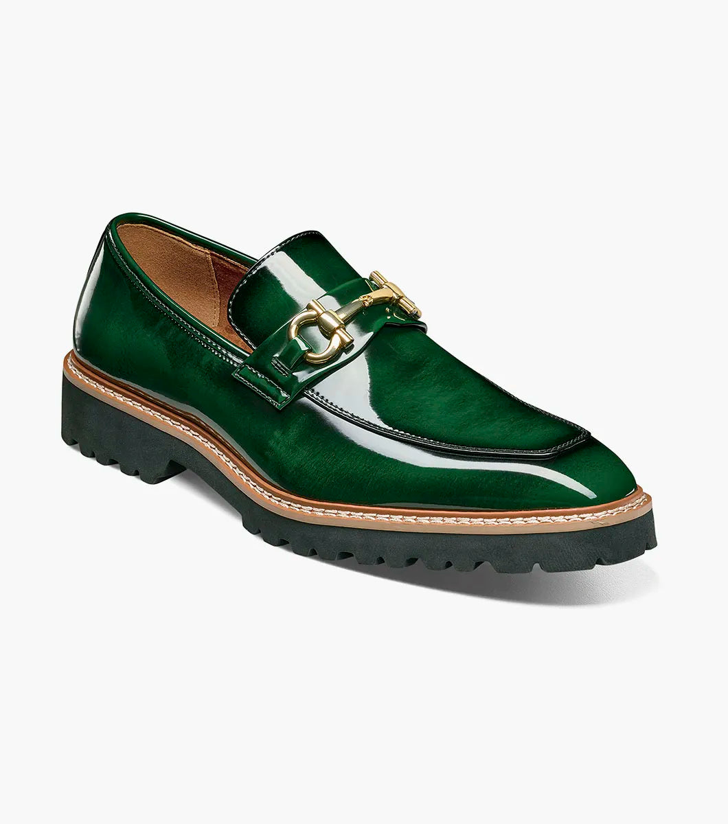 The STACY ADAMS Carabello Moc Toe Bit Slip On in green (style 25804-300) is featured against a white background. This men’s loafer showcases glossy green leather, a gold-tone bit detail, tan stitching, and a thick black lug sole for a sophisticated yet striking look that blends timeless style with modern flair.