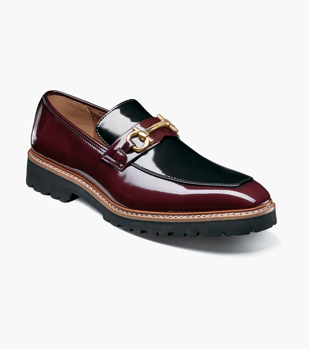 Introducing the Stacy Adams Carabello Moc Toe Bit Slip On in Burgundy Multi (style 25804-641): This STACY ADAMS loafer showcases a glossy two-tone upper in black and burgundy, accented with gold hardware across the front, a tan interior lining, and a chunky black sole. The moc toe bit design also features a plush memory foam insole for exceptional comfort.