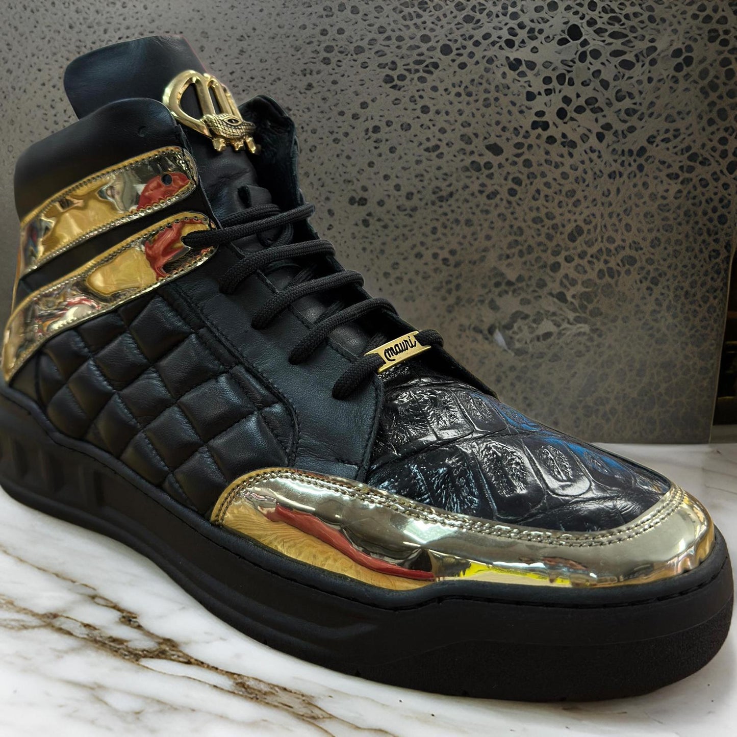 The Mauri 8499 Black/Gold Boots, featuring quilted patent leather, gold metallic accents, and a decorative lace tag, are showcased on marble. Available in sizes 9.5 and 12 only. Final sale in store from Mauri.