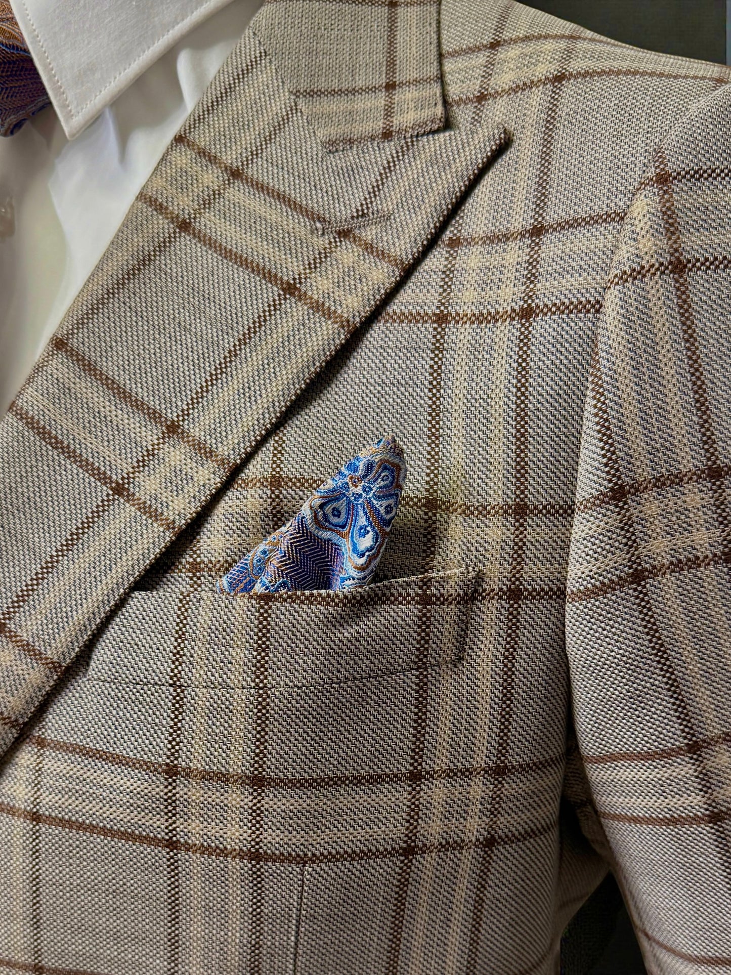 A man with gray hair and beard wears a brown plaid Tiglio Luxe Prosecco Modern Fit suit and vest, paired with a white shirt and patterned tie, standing against a plain light background.