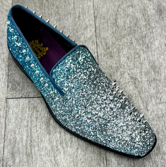 A single Exclusive Formal Dress Shoe Blue / Silver 6860 from UNIQUE DESIGN MENSWEAR, featuring a glittery blue-to-silver gradient and genuine Italian leather adorned with silver spikes, rests on a light wood floor.