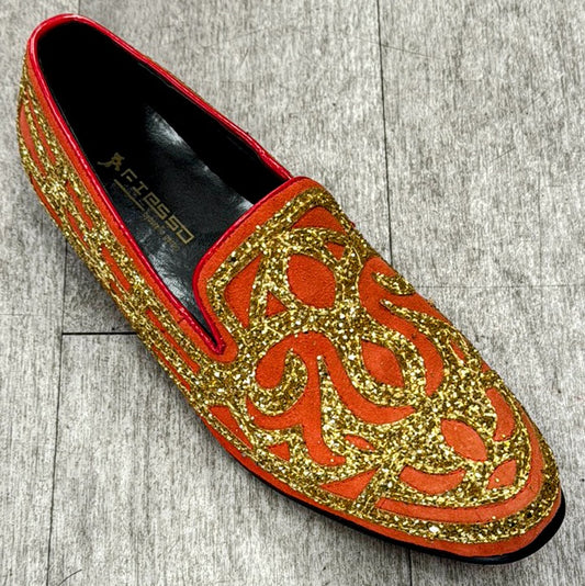 An orange slip-on shoe from UNIQUE DESIGN MENSWEAR, known as the Exclusive Formal Dress Shoe Orange / Gold FI7020, showcases intricate gold glitter patterns over a textured surface, elegantly resting on a gray wooden floor.