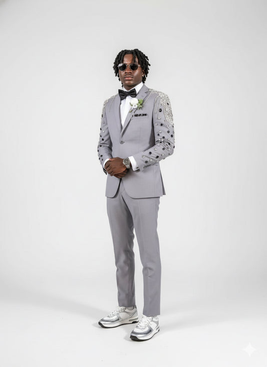 A man in the Unique Design Menswear Custom Prom Suit Grey with Black/Silver Stone Work and metallic sneakers poses against a white background, accessorizing with a bow tie and sunglasses.