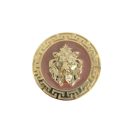 The Matiste Rose/Gold Belt Buckle 35mm B35 features a gold circular design with a raised lion head and Greek key border, exemplifying Italian craftsmanship, set against a pink background.