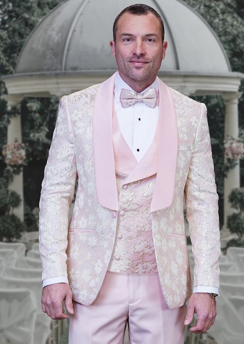 A man in a STATEMENT TIZANO BLUSH Suit by Statement Clothing stands before a garden-themed backdrop with a dome and greenery.