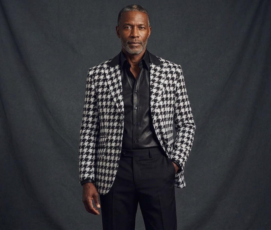 A man stands against a dark background wearing the Inserch Black White Houndstooth Blazer BL264 (FINAL SALE) over a black shirt and trousers.