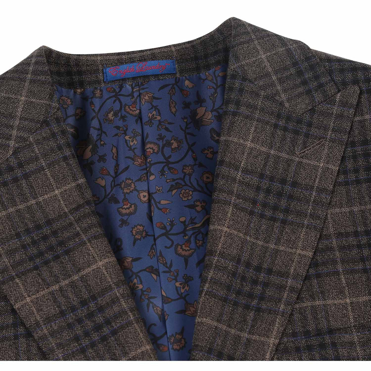 The mannequin is adorned in an English Laundry three-piece sand brown check suit, featuring a sleek jacket that drapes elegantly over a white dress shirt, complemented by a maroon polka dot tie.