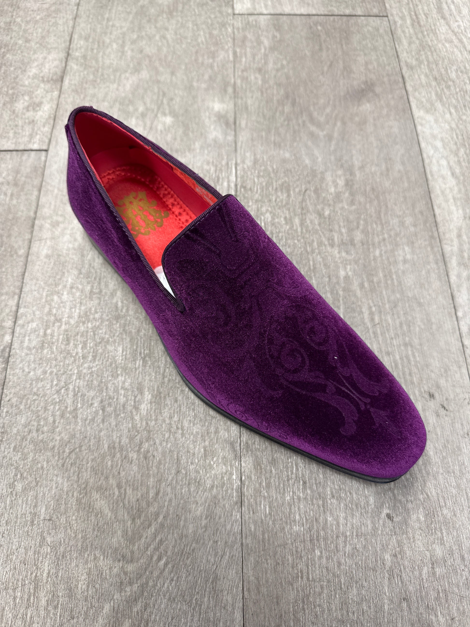 The AFTER MIDNIGHT 7017 PURPLE PAISLEY velvet slip-on, featuring a sleek buckle and subtle side stitching, rests on a wooden floor.