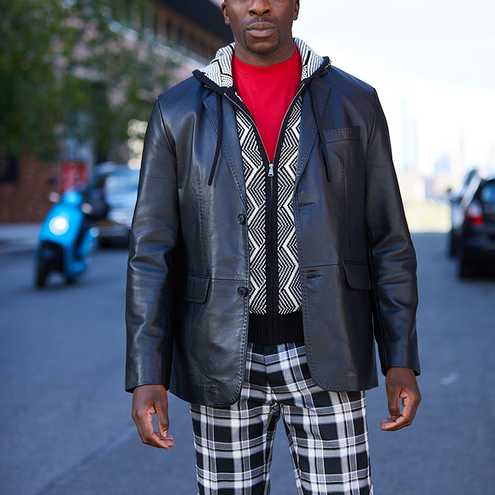 A person stands by a window wearing the Inserch Leather Blazer 600-01 Black by Inserch, paired with a black turtleneck sweater and red plaid pants.