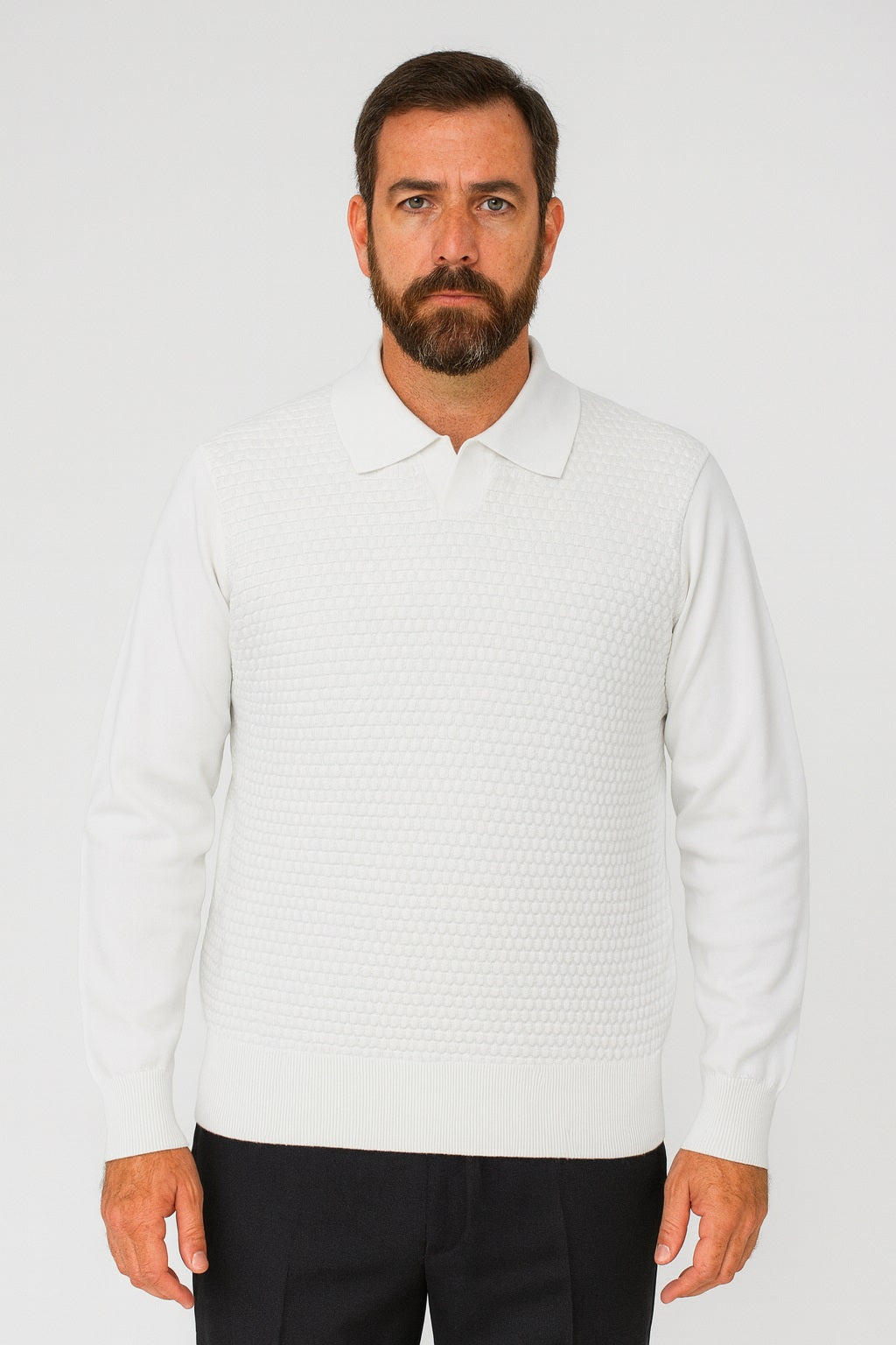 A bearded man faces forward in a plain white setting, wearing the Bassiri Long Sleeve Collar Neck White Sweater 640 by Bassiri and dark pants.