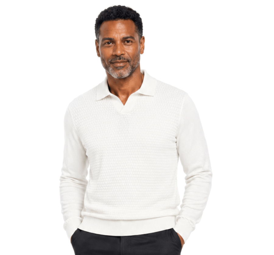 A bearded man faces forward in a plain white setting, wearing the Bassiri Long Sleeve Collar Neck White Sweater 640 by Bassiri and dark pants.