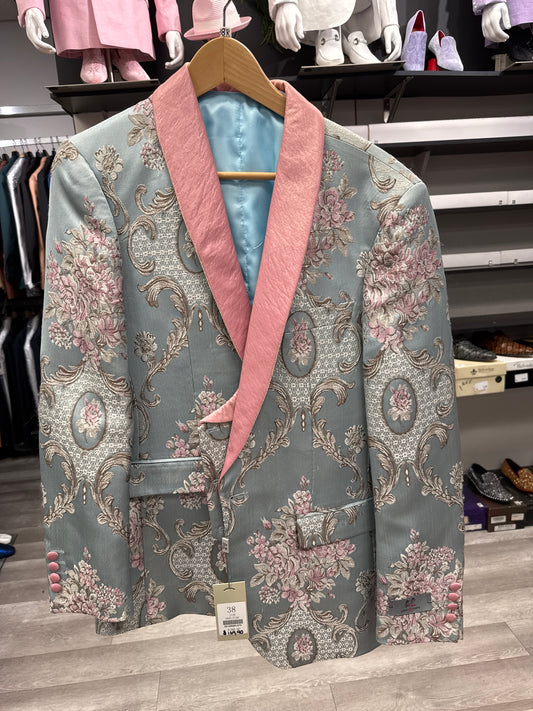 The EJ SAMUEL JACKET 20 CLEARANCE, a men's blazer with a silver and pink floral brocade pattern on light blue fabric and a pink shawl collar, is displayed on a wooden hanger in the clothing store. Please note: this item is final sale—no exchanges or returns.