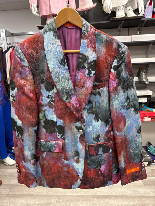 The EJ SAMUEL JACKET 18 CLEARANCE, featuring a vibrant abstract pattern in red, blue, black, and gray, is displayed on a wooden hanger in the store. Please note: this item is final sale—no returns or exchanges will be accepted.