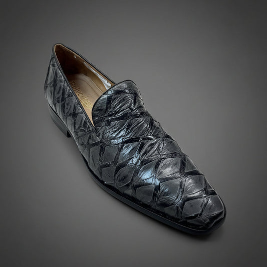 A single black, shiny, textured leather BELVEDERE Belvedere Shoe 6 (Size 9 Only) sits on a wooden surface, with folded clothes in the background. This item is FINAL SALE—no exchanges or returns.