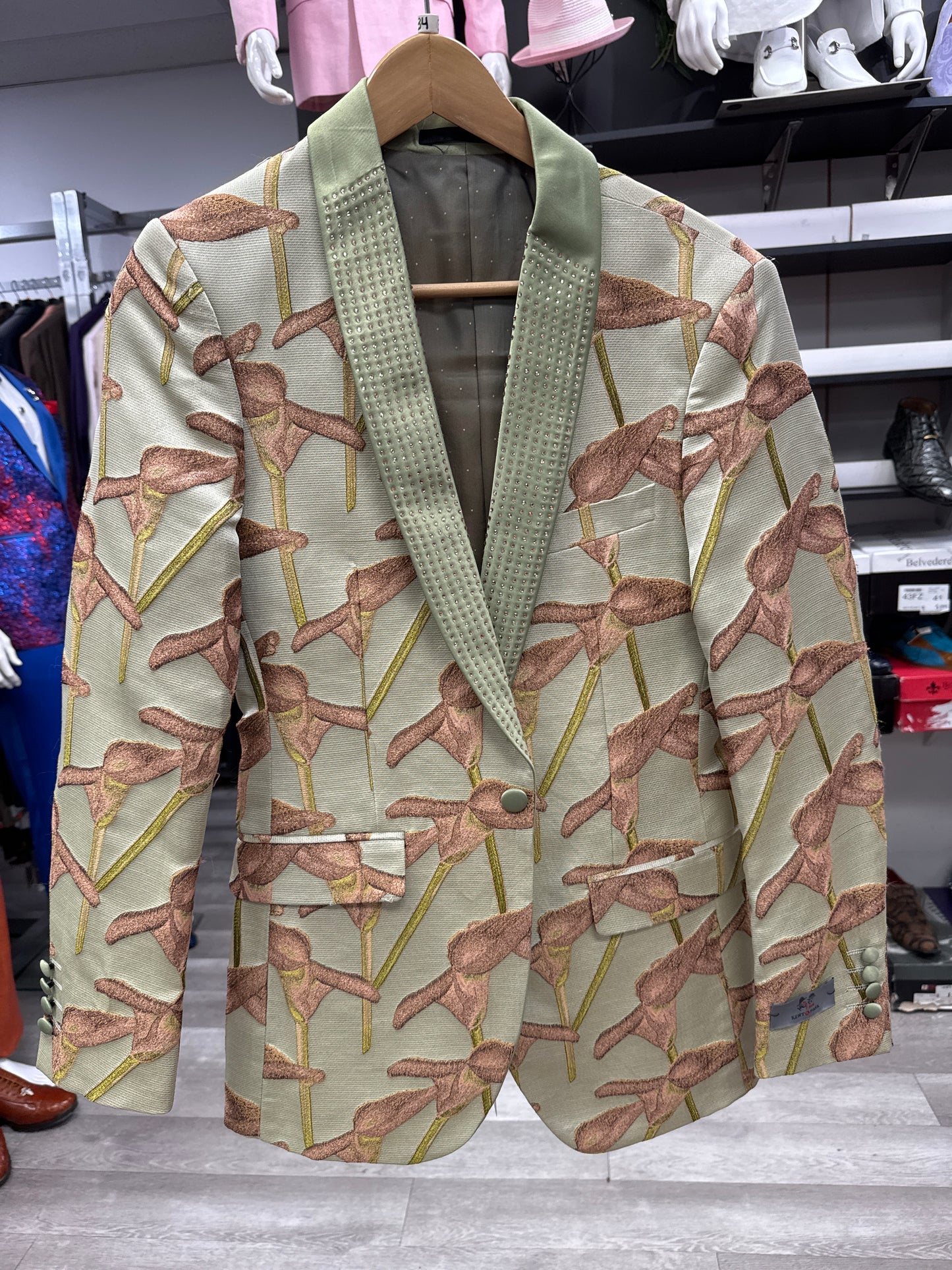JACKET 16 CLEARANCE by EJ SAMUEL—a beige blazer with green lapels, featuring an all-over pattern of brown flamingos, displayed on a wooden hanger in a clothing store. Please note: final sale—no exchanges or returns.