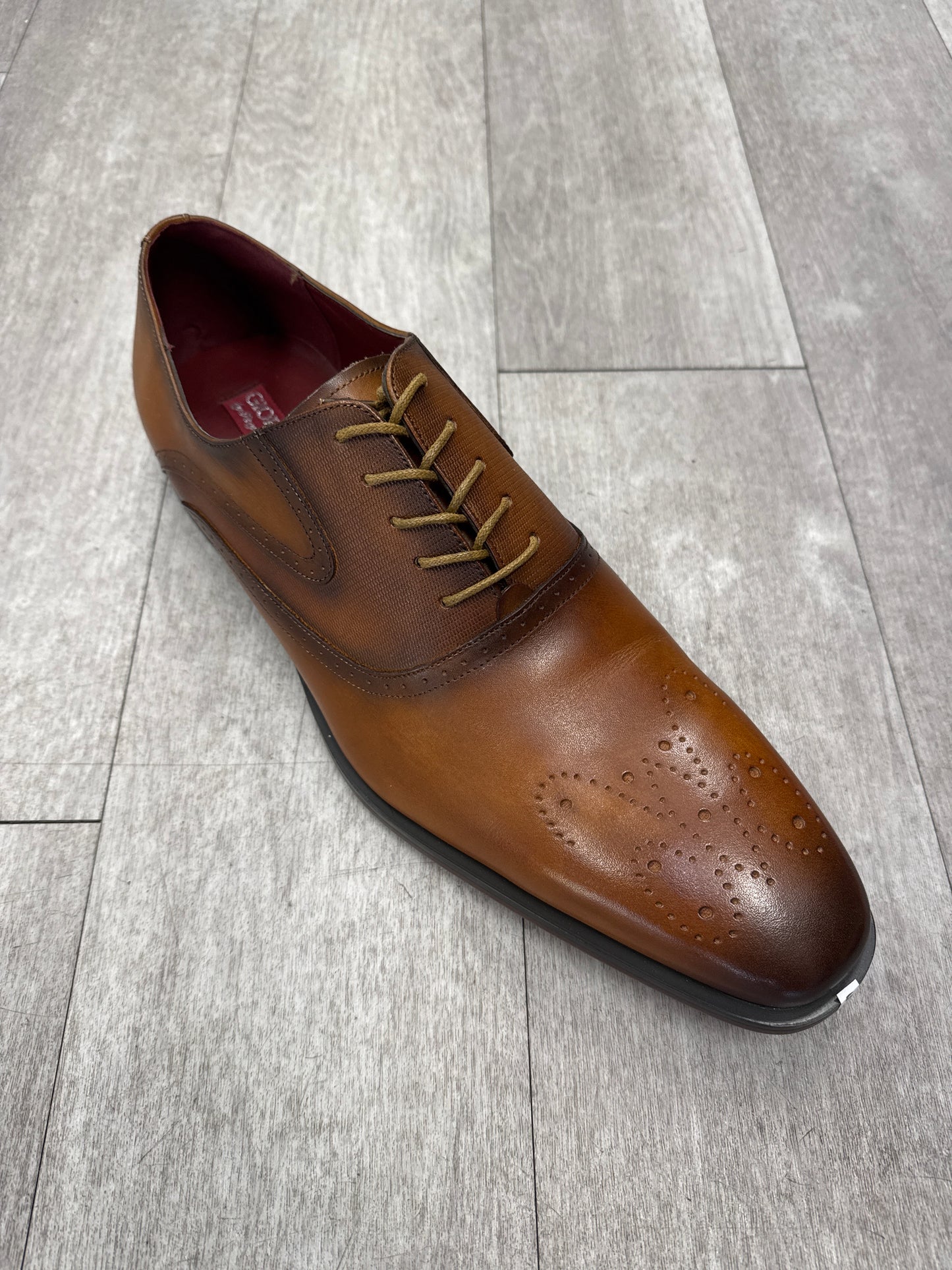 A Fiesso brown leather Shoe 92 in size 15, featuring decorative perforations on the toe, is elegantly displayed on a light wood floor. Please note, this item is FINAL SALE and cannot be returned.