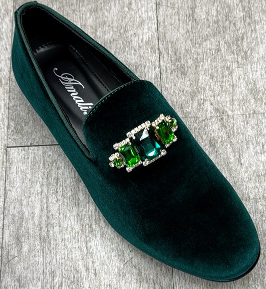 The Exclusive Formal Dress Shoe Green TIAGO by UNIQUE DESIGN MENSWEAR, a luxurious green velvet shoe crafted in Italy and embellished with a rectangular brooch of green and silver gemstones, gracefully sits on a wooden floor.