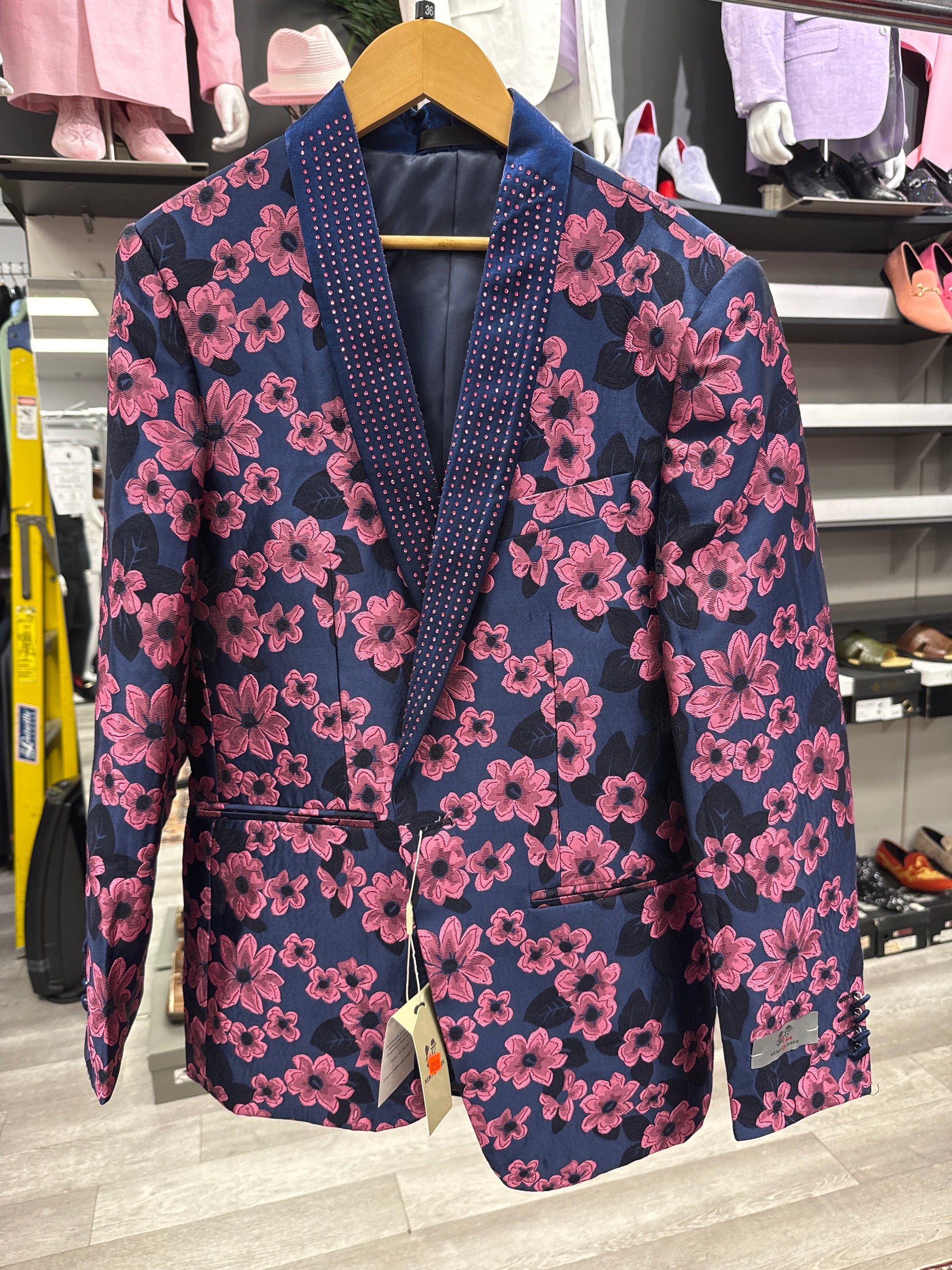 A JACKET 11 CLEARANCE by EJ SAMUEL—a blue blazer featuring a pink floral pattern and dark lapels—is displayed on a wooden hanger in the store; please note, this is a final sale item and cannot be returned or exchanged.
