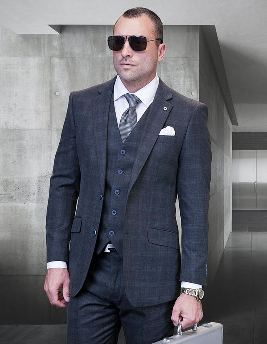 A man in the STATEMENT CLOTHING | ALGANI-CHARCOAL Italian wool suit by Statement Clothing, with a double-breasted vest, white shirt, tie, sunglasses, and a silver briefcase stands in a modern office hallway.