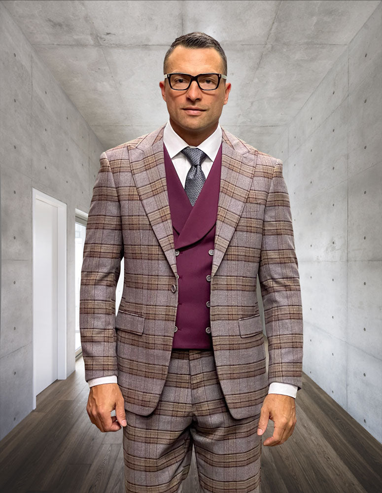 A man wearing glasses and a Statement Clothing STATEMENT CLOTHING | AMICCI-BURGUNDY modern fit plaid peak lapel suit with a maroon vest stands in a sleek concrete hallway with wooden floors.