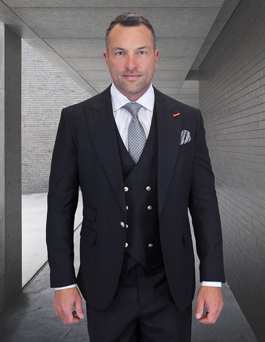 A man wearing the STATEMENT CLOTHING | AMIRI-BLACK suit, white shirt, and patterned tie from Statement Clothing stands in a sleek gray concrete hallway.