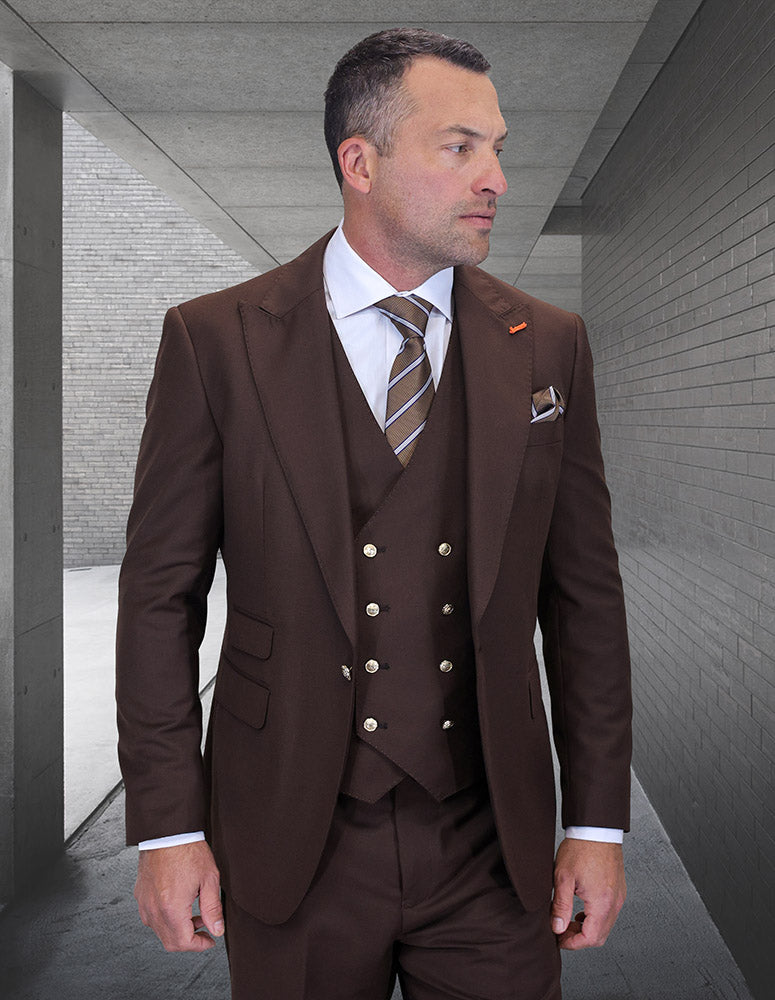 A man in the STATEMENT CLOTHING | AMIRI-BROWN modern fit suit by Statement Clothing, paired with a striped tie, stands in a sleek gray concrete hallway, looking to his left.