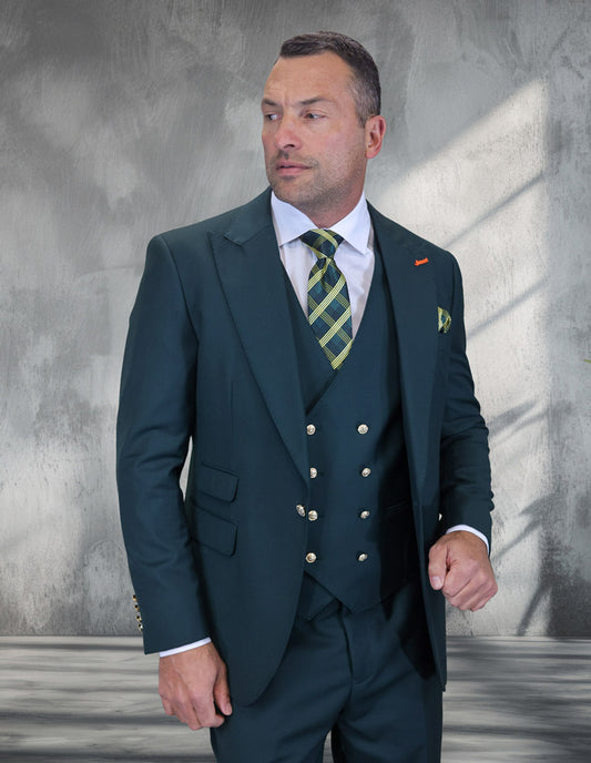 A man in a STATEMENT CLOTHING | AMIRI-HUNTER Italian wool hunter suit by Statement Clothing pairs it with a white shirt and green plaid tie, standing before a textured gray wall and looking left.