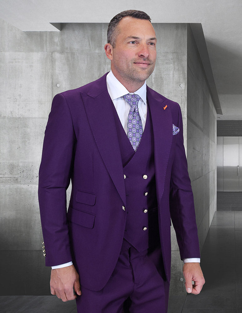 A man in the STATEMENT CLOTHING | AMIRI-PLUM Italian Super 200's wool suit by Statement Clothing, paired with a patterned tie, stands indoors against gray concrete walls.