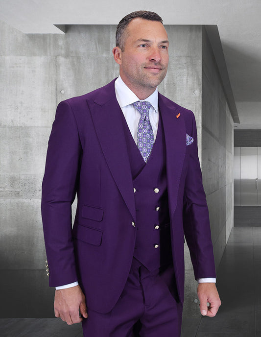 A man in the STATEMENT CLOTHING | AMIRI-PLUM Italian Super 200's wool suit by Statement Clothing, paired with a patterned tie, stands indoors against gray concrete walls.
