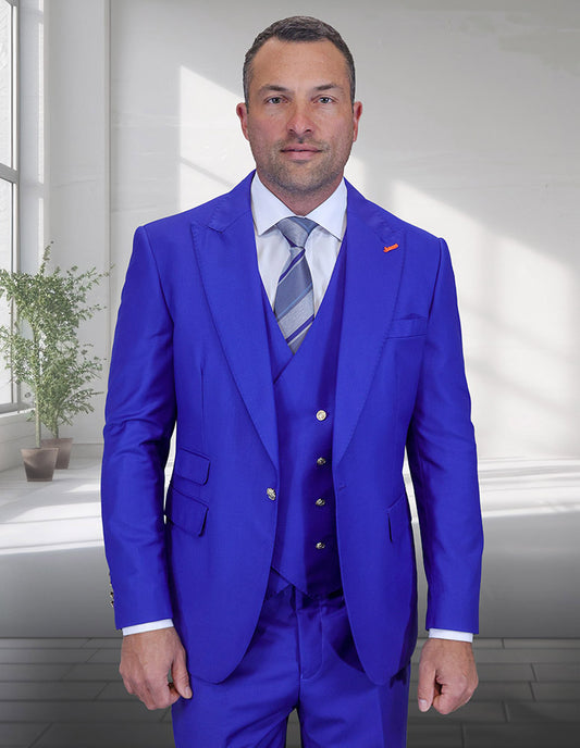 A man stands indoors with a plant and large windows behind him, wearing the Statement Clothing AMIRI-ROYAL bright blue Super 200's Italian Wool Suit, paired with a white shirt and striped tie.