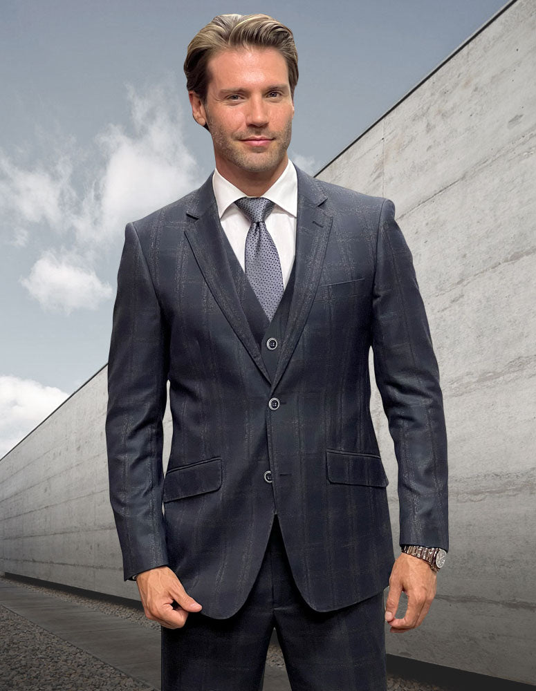 A man in a STATEMENT CLOTHING | ANGEL-1-BLACK modern-fit Italian wool suit by Statement Clothing, paired with a white shirt and tie, stands outdoors before a modern concrete wall under a cloudy sky.