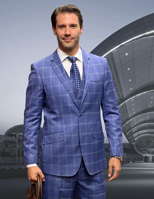 A man wearing Statement Clothing's ANGEL-3-INDIGO blue checked Italian wool suit with flat front pants holds a brown bag, standing before a modern glass and steel curved building.