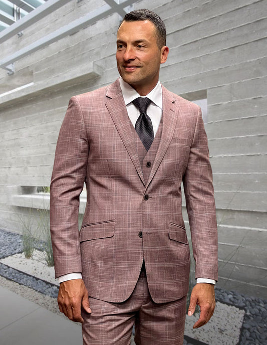 A man stands indoors by a concrete wall, wearing the STATEMENT CLOTHING | ANGEL-3-MAUVE modern fit Italian wool suit from Statement Clothing with flat front pants, a white dress shirt, and black tie.