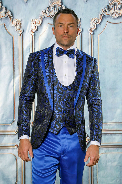 Wearing the Insomnia MANZINI ASHER 3-Piece Slim Fit Royal Tuxedo Prom Suit, featuring shiny satin and a paisley pattern, a person stands before an ornate backdrop.