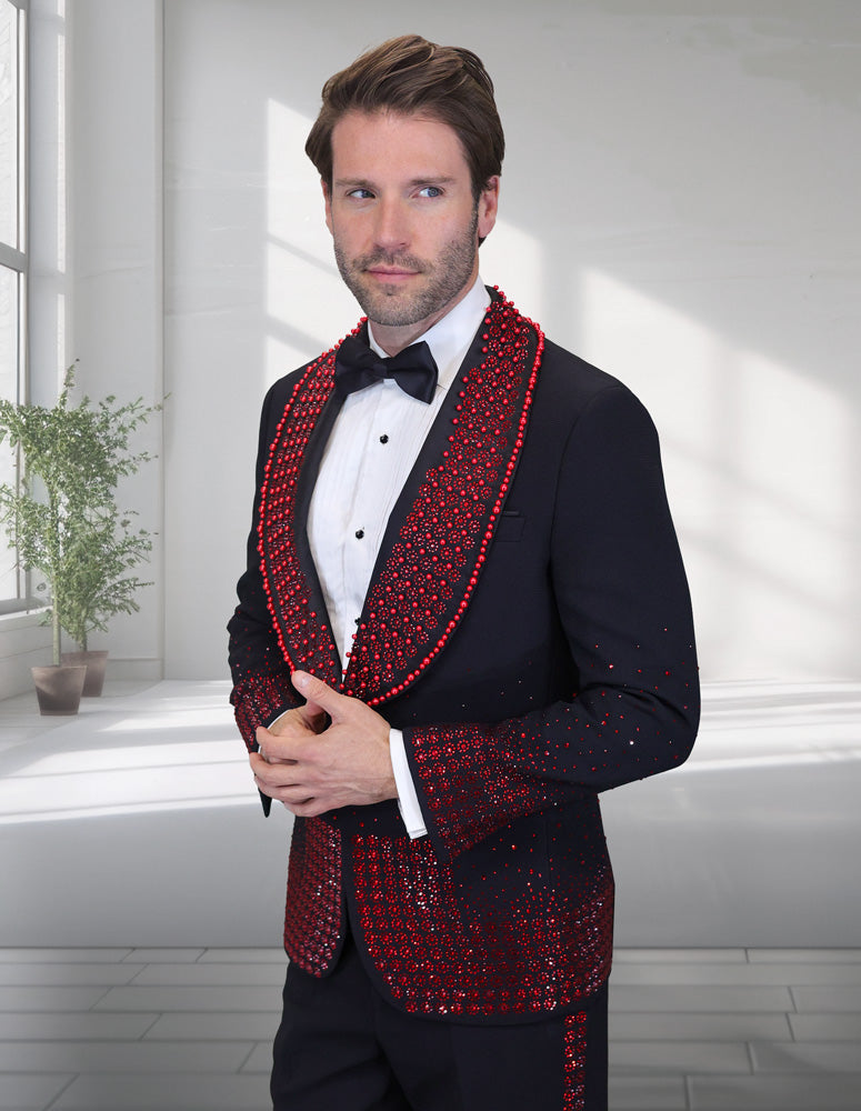 A man wearing the STATEMENT CLOTHING AWARD-BLACK WITH RED STONES tuxedo by Statement Clothing stands indoors near a window and potted plant, looking to the side.