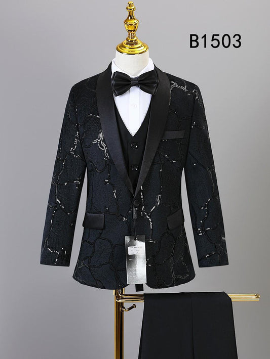 The BOY SUIT 5-PC SET B1503 by Unique Design Menswear features a black patterned tuxedo with satin lapels, white shirt, black bow tie, vest, and matching trousers—perfect boys' formal wear. Displayed on a mannequin with trousers below.