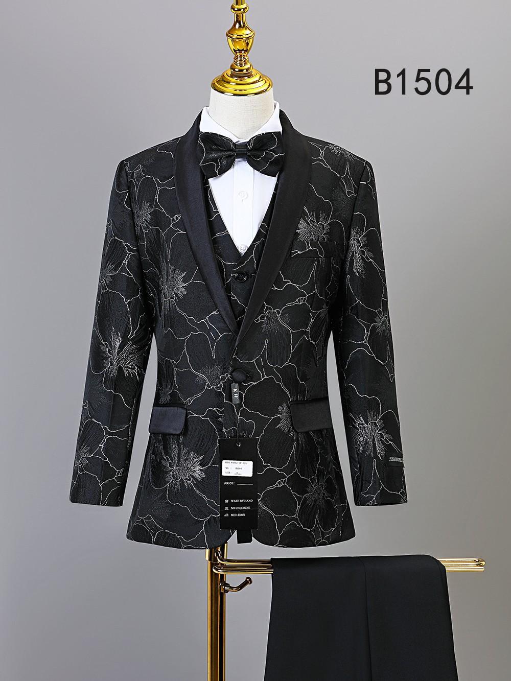 The Unique Design Menswear BOY SUIT 5-PC SET B1504 features a black floral-patterned suit with matching vest and bow tie, elegantly displayed on a mannequin. Includes black dress pants—ideal for boys’ formal occasions.
