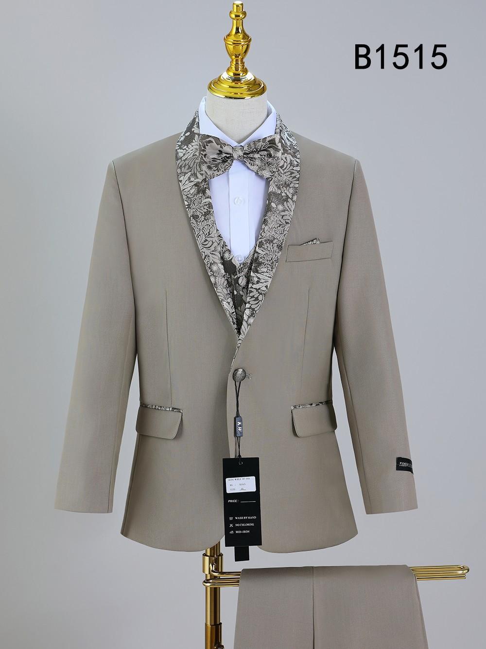 The BOY SUIT 5-PC SET B1515 by Unique Design Menswear is a beige boys' suit with floral-patterned lapels and bow tie, displayed on a mannequin with matching pants draped over a stand.