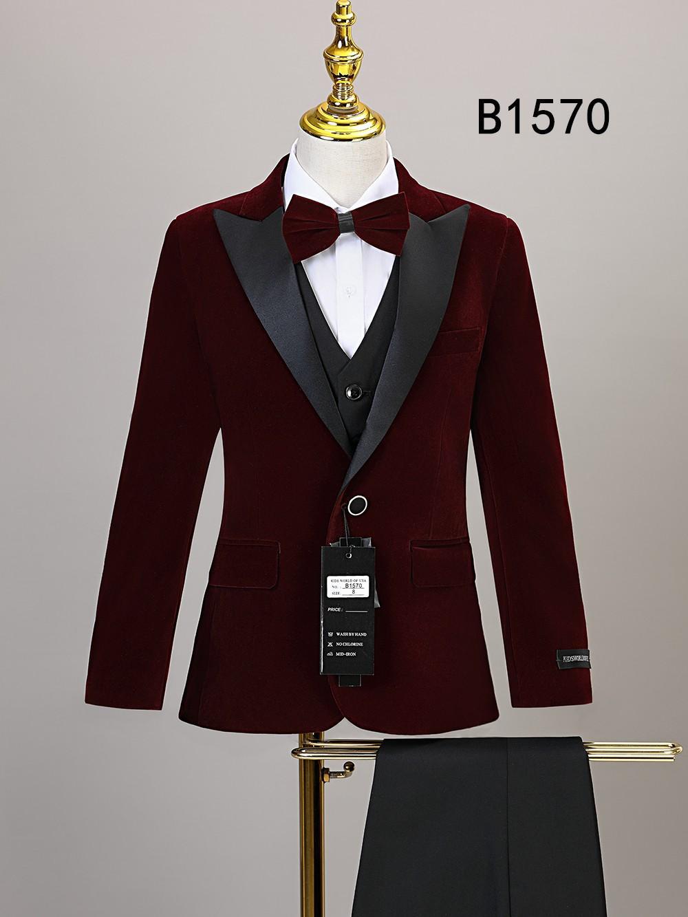 The BOY SUIT 5-PC SET B1570 by Unique Design Menswear features a burgundy velvet jacket with black satin lapels, bow tie, vest, and pants—perfect for boys' formal wear. Displayed on a mannequin.