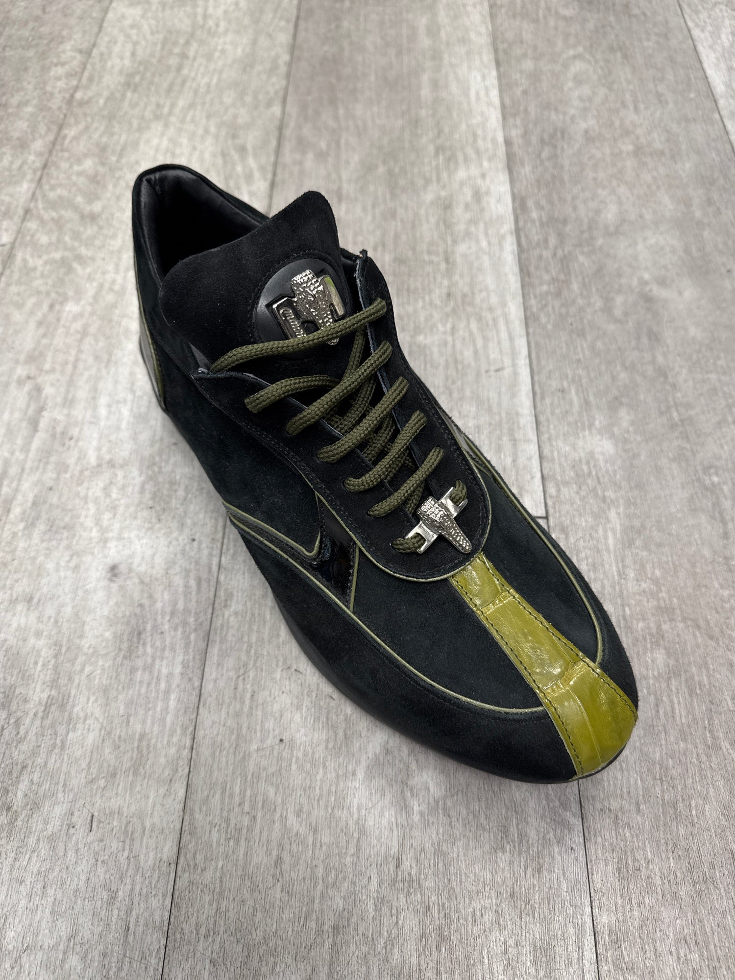 The Mauri 8464 Black/Olive sneaker (Size 8.5 Only) features suede with a glossy green stripe, elegantly placed on a wooden floor. FINAL SALE - NO EXCHANGE, NO RETURN.