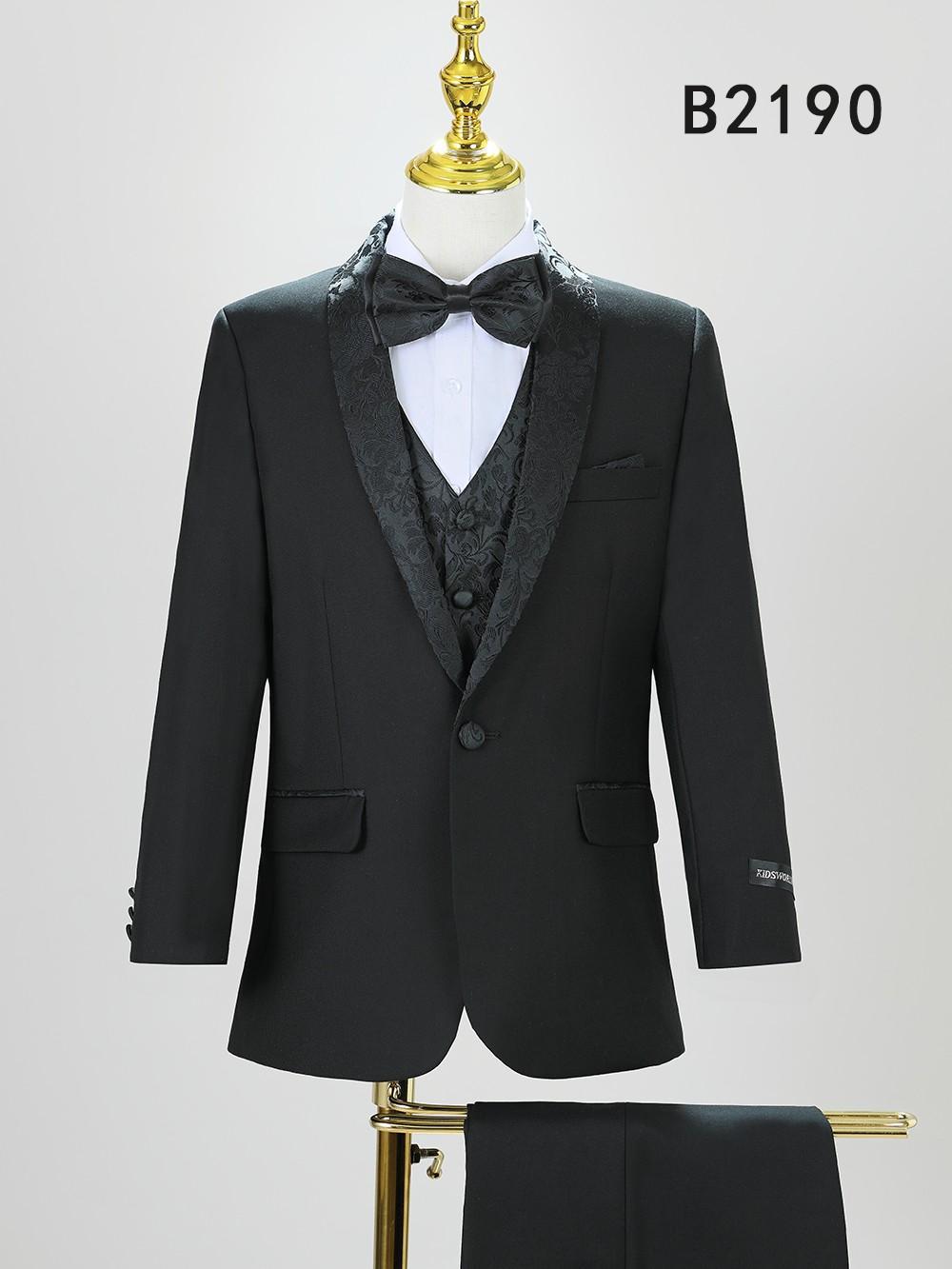 The BOY SUIT 5-PC SET B2190 by Unique Design Menswear features a black suit with patterned shawl lapel, matching vest, white shirt, and black bow tie on display. Ideal for boys' formal wear.