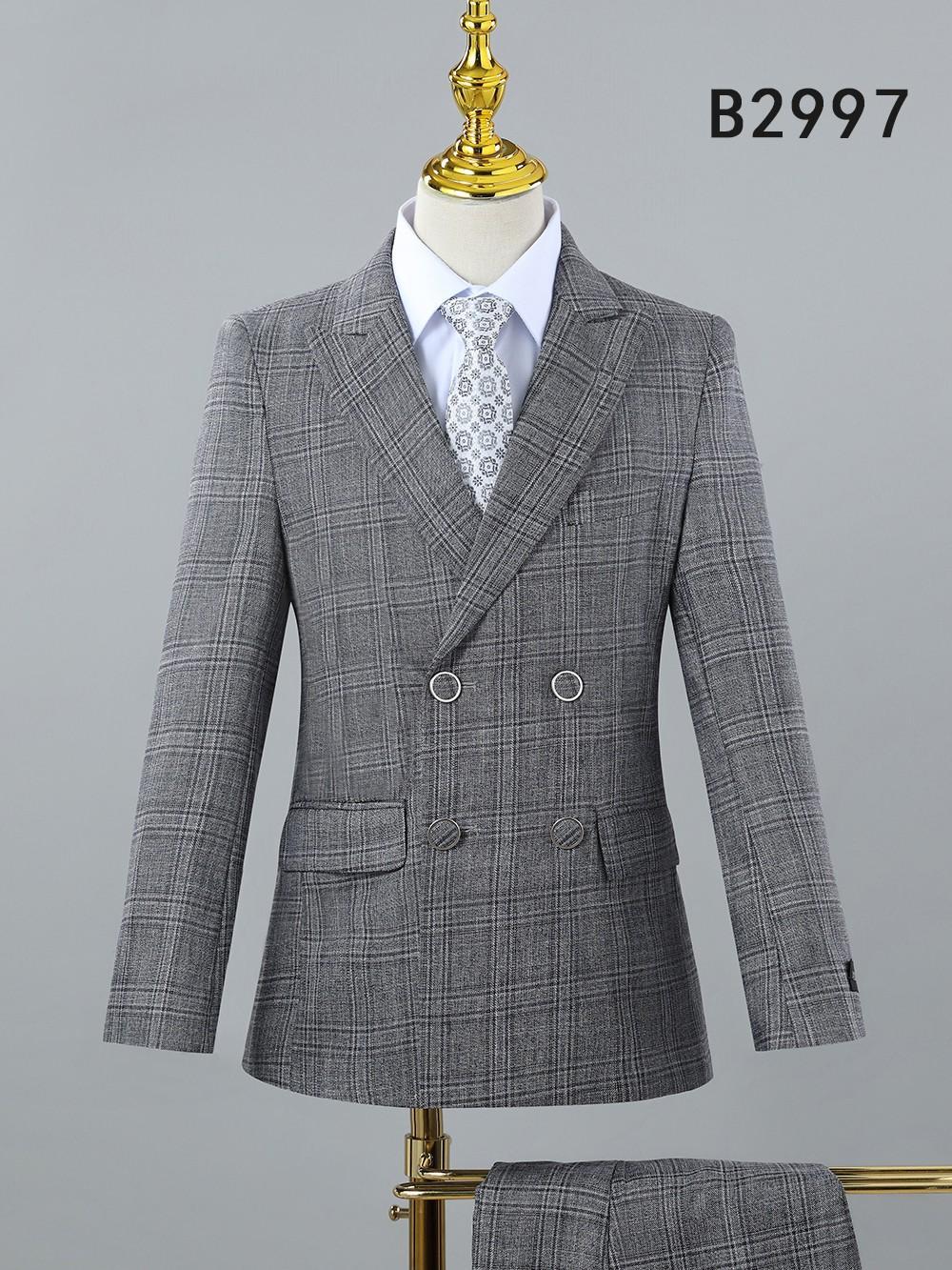 The BOY SUIT 5-PC SET B2997 by Unique Design Menswear, shown on a mannequin with a gray plaid double-breasted jacket, peak lapels, white shirt, and patterned tie, is ideal for boys’ formal occasions. Code B2997 appears in the top right corner.