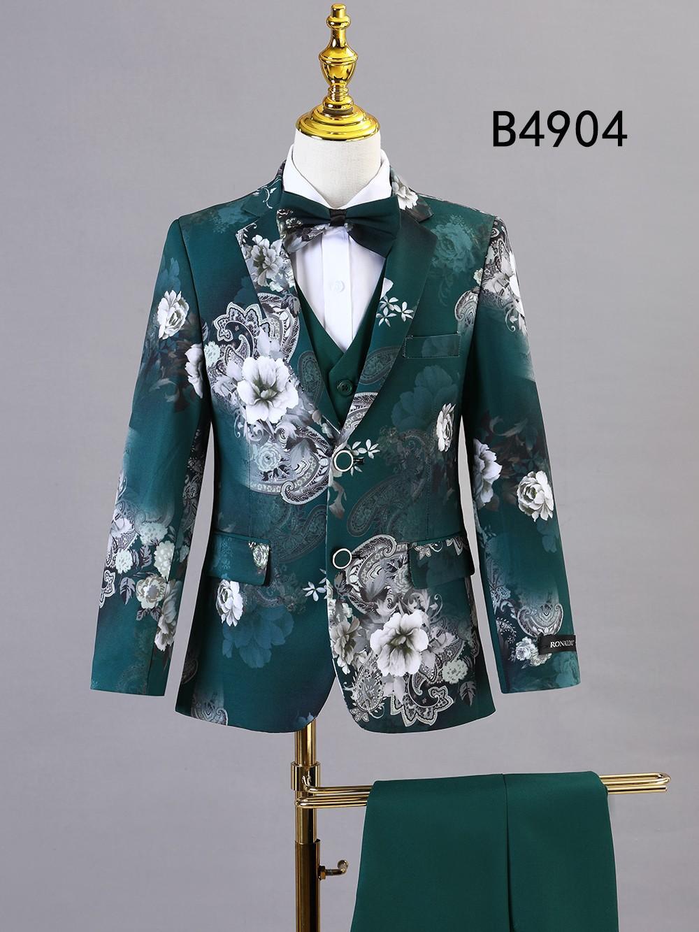 Showcased on a mannequin, the BOY SUIT 5-PC SET B4904 by Unique Design Menswear features a green floral pattern with matching vest, white shirt, black bow tie, and coordinating trousers—ideal formal wear for boys.