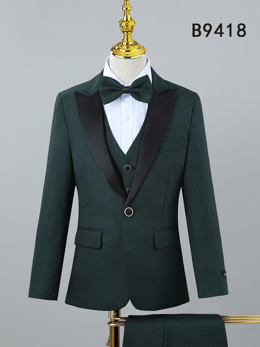 The Unique Design Menswear BOY SUIT 5-PC SET B9418 features a dark green boys’ formal suit with black satin lapels, white dress shirt, and matching bow tie, stylishly displayed on a mannequin.