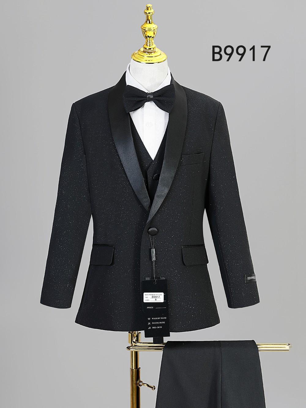 The Unique Design Menswear BOY SUIT 5-PC SET B9917 features a black suit with satin lapels, white dress shirt, black bow tie, and pants—ideal for boys' formal wear. Displayed on a mannequin; pants shown draped on a stand.