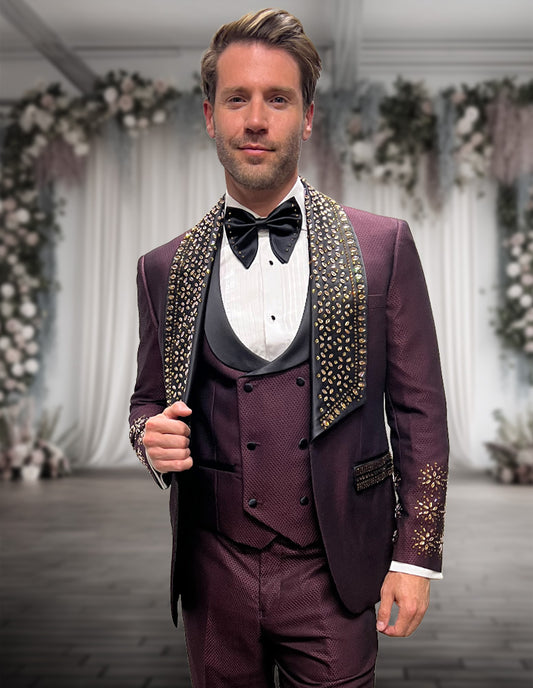 A man wears the STATEMENT CLOTHING | BELLA-BURGUNDY modern fit Italian tuxedo by Statement Clothing, standing indoors on a wooden floor with floral arrangements and white drapery in the background.