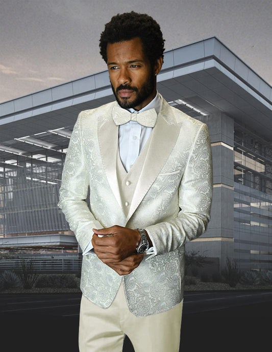 A man wears the STATEMENT CLOTHING | BELLAGIO-4-OFFWHITE slim fit tuxedo from Statement Clothing, featuring a white patterned design with a bow tie and flat front pants, standing before a modern glass office building.