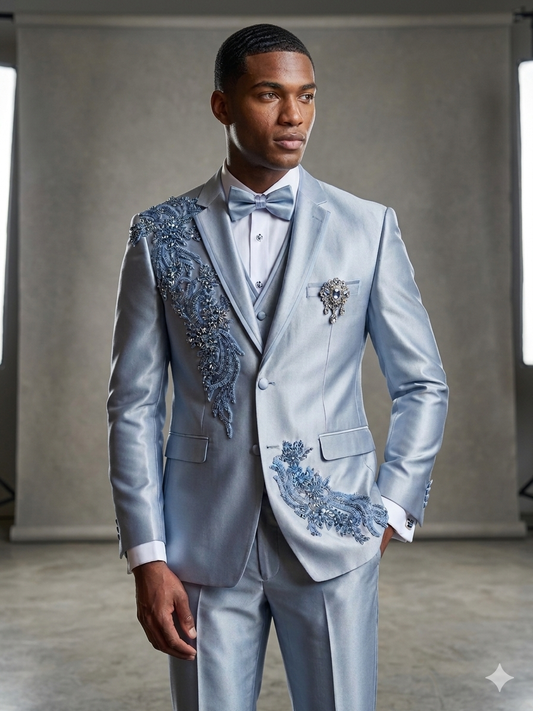 A man wears the Unique Design Menswear Custom prom suit in light blue rhinestone with intricate blue floral embroidery and beadwork, bow tie included, standing in a studio setting.